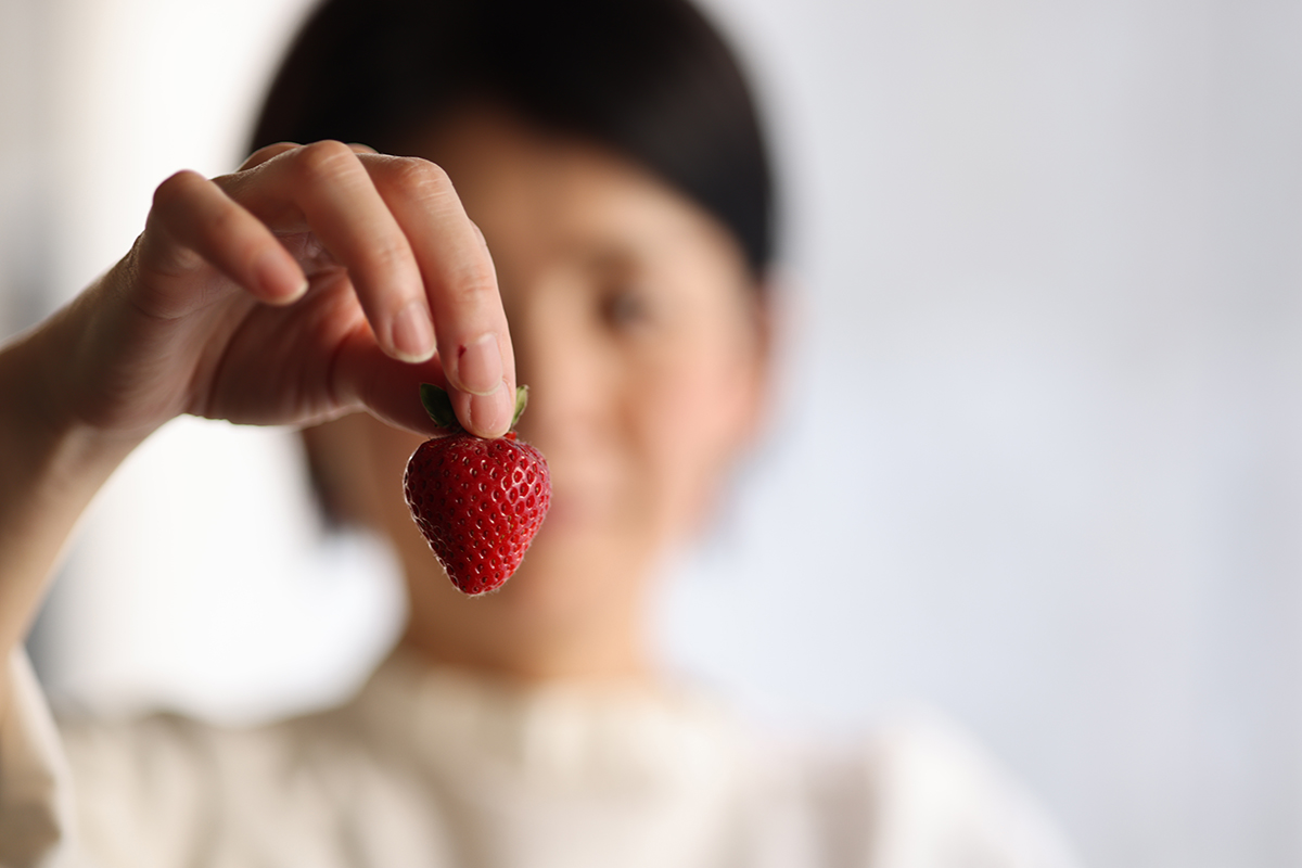 1粒のいちごとその後ろにぼけた女性の姿