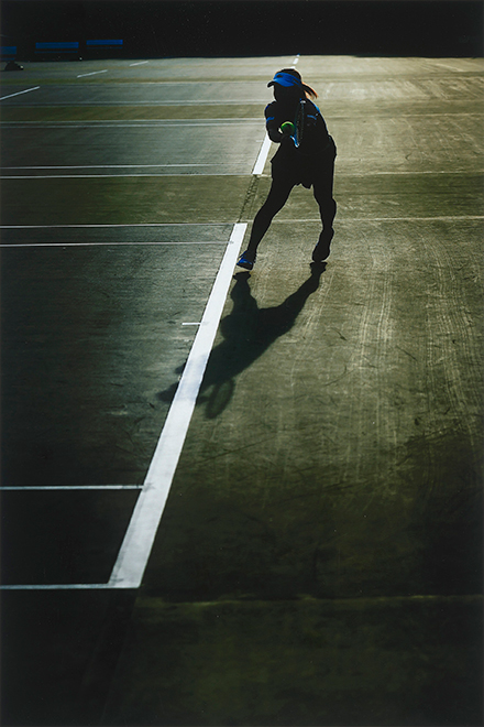 逆光のテニスコートでラケットを構える女性
