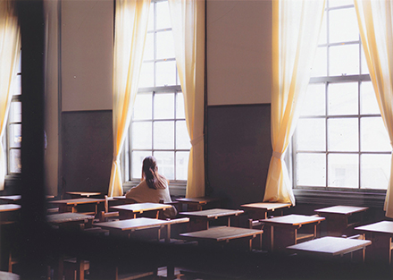 大きな窓の教室で一人外を見ている女性