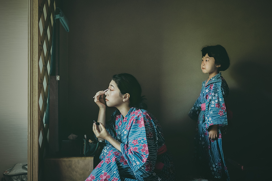 鏡に向かって化粧をしている女性とそれを見ている子供